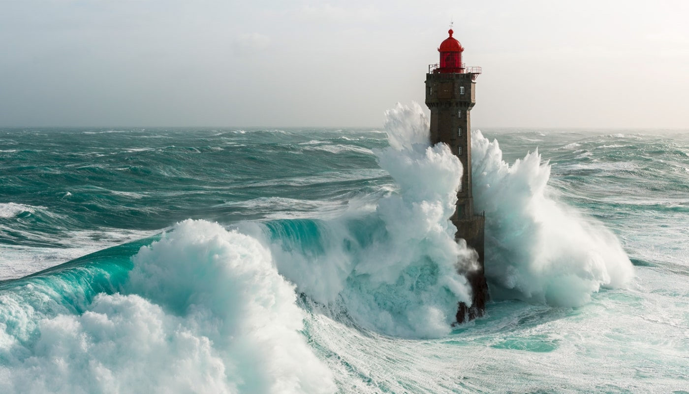 Heldenbild mit einer großen Welle, die während eines Sturms um einen Leuchtturm bricht.