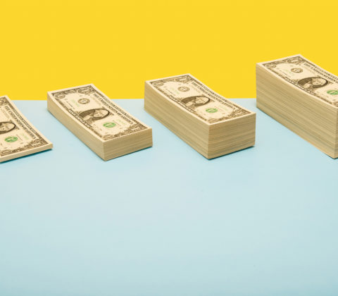 Bühnenbild mit gelbem und hellblauen Hintergrund mit verschieden großen Stapeln an Geldscheinen